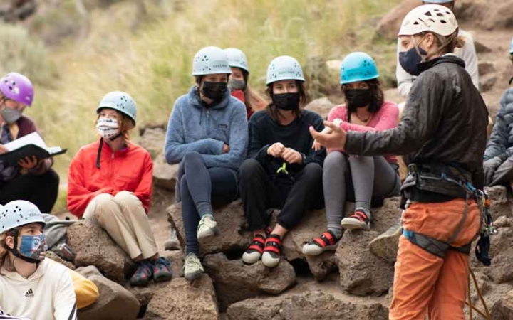 an outward bound instructor gives direction to a students preparing to rock climb